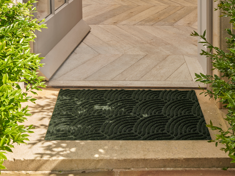 dunkelgrüne Fußmatte mit 3D-Struktur im Außenbereich vor der Tür liegend