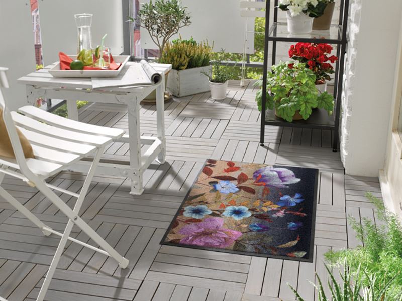 Fußmatte in schwarz mit buntem, violettem Blumenmotiv auf dem Balkon