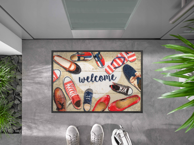 Fußmatte mit Schuhen und Schrift "welcome" vor der Tür