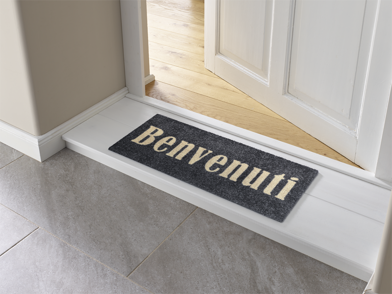 graue Fußmatte mit Schrift "Benvenuti" vor der Tür