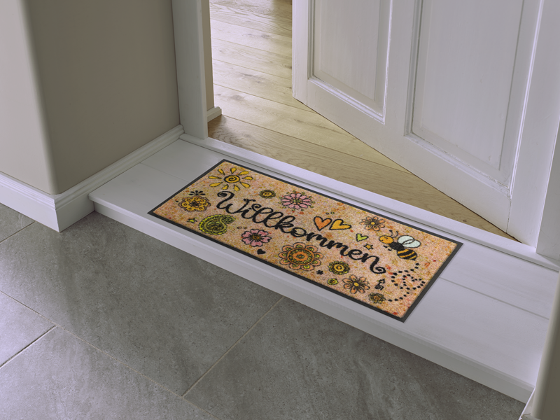 Fußmatte mit freundlichen Motiven und Schriftzug "Willkommen" vor der Tür
