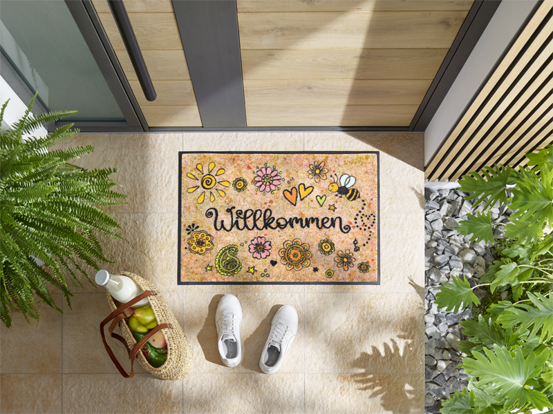 Fußmatte mit freundlichen Motiven und Schriftzug "Willkommen" vor der Tür