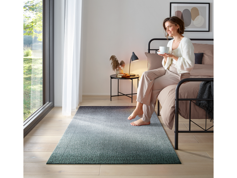 Fußmatte mit grün-schwarzer und dezenter Musterung im Schlafzimmer mir einer Frau