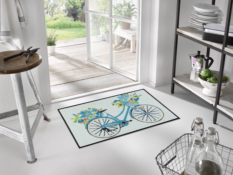 hellblaue Fußmatte mit Fahrrad und Blumen im Eingangsbereich