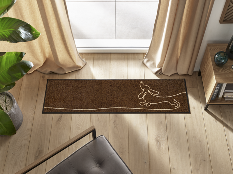 braune Fußmatte mit liniengezeichnetem Dackel-Hund vor dem Fenster