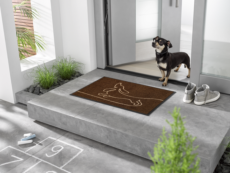 braune Fußmatte mit liniengezeichnetem Dackel-Hund vor der Tür