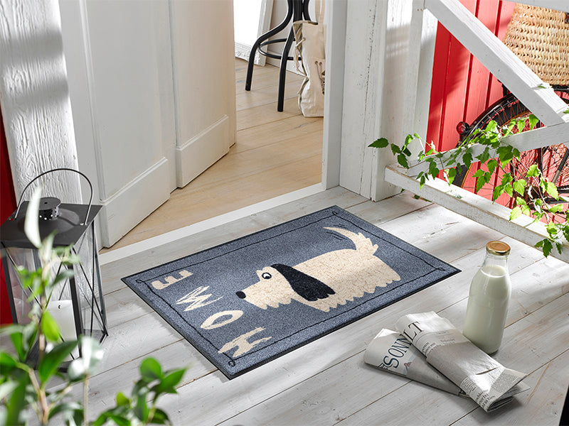 Fußmatte mit Hundemotiv und Schrift "HOME" vor der Tür