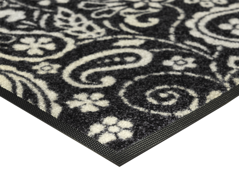 Eckansicht der Fußmatte schwarz mit weißem verschnörkeltem Blumenmuster