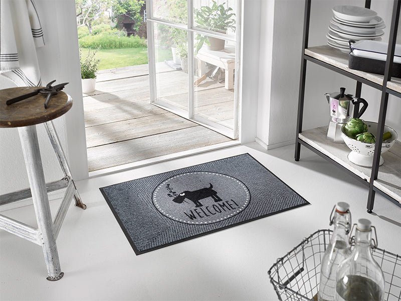 graue Fußmatte mit Schriftzug "WELCOME!" und Hundemotiv im Eingangsbereich