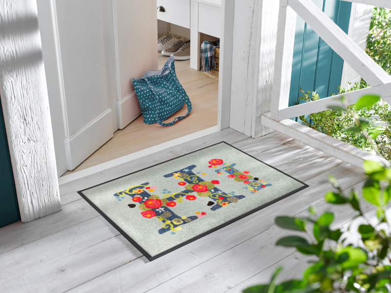 Fußmatte mit Schriftzug "HI" mit Blumen geschmückt vor der Tür
