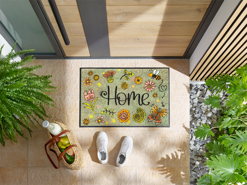 Fußmatte mit Blütenmotiven, Biene und Schriftzug "Home" vor der Eingangstür