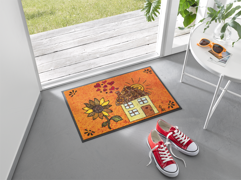 Fußmatte mit gezeichnetem Haus und einer großen Sonnenblume im Eingangsbereich