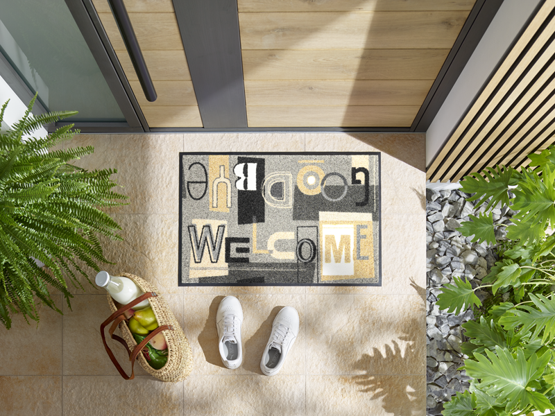 Fußmatte mit Schrift "Welcome Goodbye" in Beige und Grautönen vor der Eingangstür